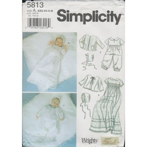 Puede incluir: Patrón de costura Simplicity 5813 para ropa de bebé. El patrón incluye opciones para un vestido, una chaqueta, un gorro y un pelele. La imagen muestra un bebé con un vestido y un pelele. El patrón está diseñado por Kacca Z.