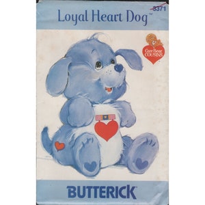 May include: A blue and white Care Bear Cousins sewing pattern featuring a dog with a heart on its chest. The pattern is titled "Loyal Heart Dog" and has the number 3371 on it.