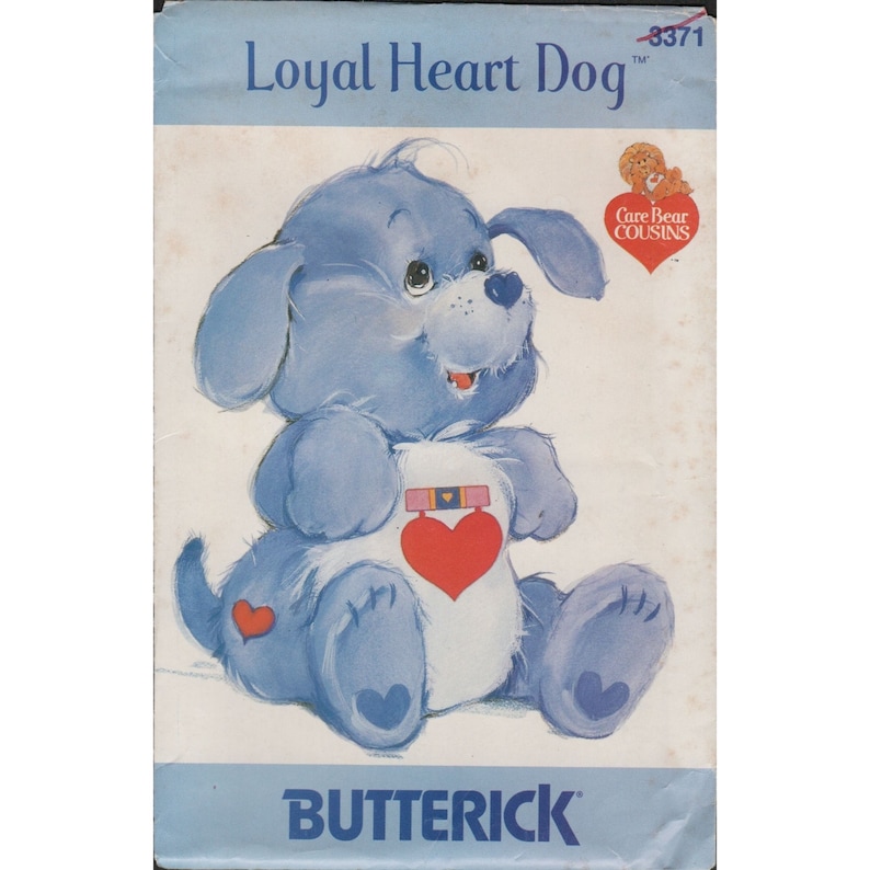 May include: A blue and white Care Bear Cousins sewing pattern featuring a dog with a heart on its chest. The pattern is titled "Loyal Heart Dog" and has the number 3371 on it.
