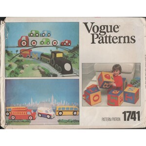May include: Vogue Patterns 1741. The image shows a pattern cover with illustrations of toy vehicles and alphabet blocks. The top illustration features a train and cars. The bottom illustration shows a fire truck, mail truck, and bus. A child is playing with alphabet blocks.