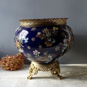 May include: A large, round, cobalt blue ceramic planter with a gold floral design and a gold metal stand with three legs.