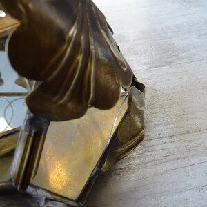 May include: A brass lantern with a decorative floral design. The lantern has a glass panel and is in a worn condition.