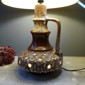 May include: A brown and white ceramic table lamp with a round base and a handle. The base has a textured surface with holes and the lampshade is white.