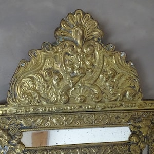 Puede incluir: Espejo dorado ornamentado con dise&ntilde;os detallados de flores y volutas. El espejo tiene forma rectangular con una parte superior decorativa. El marco est&aacute; ricamente adornado con patrones en relieve, creando una est&eacute;tica vintage.
