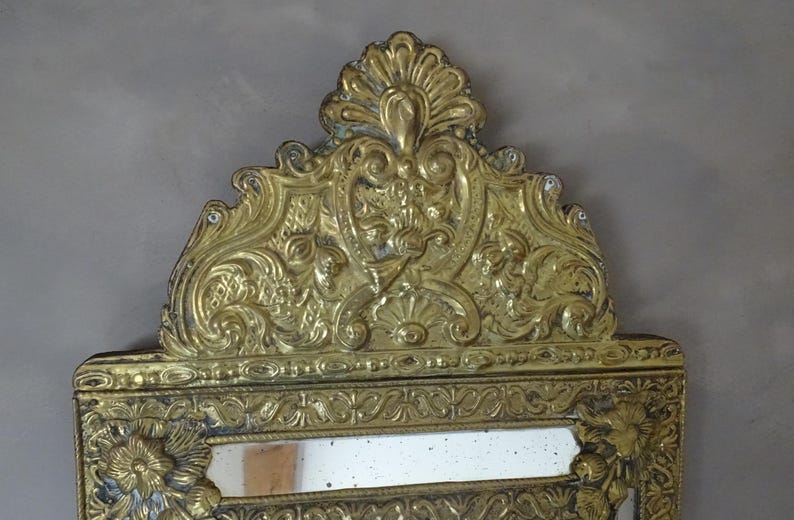 Puede incluir: Espejo dorado ornamentado con dise&ntilde;os detallados de flores y volutas. El espejo tiene forma rectangular con una parte superior decorativa. El marco est&aacute; ricamente adornado con patrones en relieve, creando una est&eacute;tica vintage.