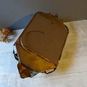 May include: A gold-toned metal wall mirror with a unique, abstract design. The mirror has a brown backing and a wire hanging loop.