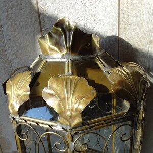 May include: A gold metal lantern with a glass top and ornate metal detailing. The lantern has a decorative design with a floral motif.