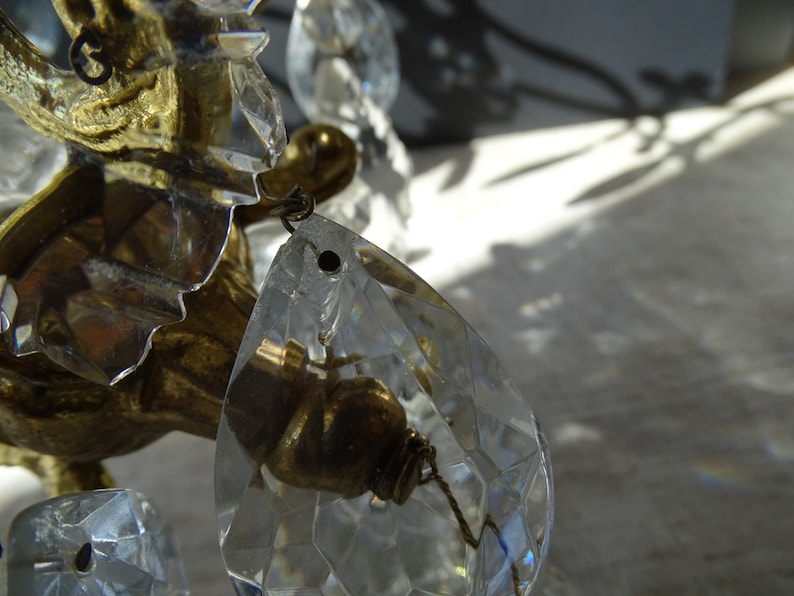 Puede incluir: Primer plano de una l&aacute;mpara de ara&ntilde;a vintage con colgantes de cristal transparente en forma de l&aacute;grima y detalles met&aacute;licos dorados. Los cristales est&aacute;n facetados, reflejando la luz. La l&aacute;mpara de ara&ntilde;a tiene un dise&ntilde;o ornamentado.