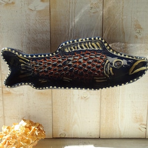 May include: A ceramic fish-shaped dish with a dark blue glaze. The dish features a textured pattern in shades of red and brown, with white dotted accents along the edges. The fish has a detailed eye and fin design, ideal for serving appetizers or as a decorative piece.