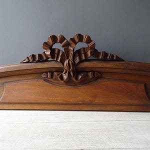 May include: A carved wooden architectural element, possibly a headboard or decorative trim. The piece features a central bow design with detailed carving and a warm brown finish. The overall design is symmetrical and ornate.