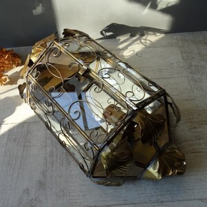 May include: A gold-toned metal and glass display case with ornate scrollwork and leaf accents. The case has a hinged lid and is perfect for displaying small items.