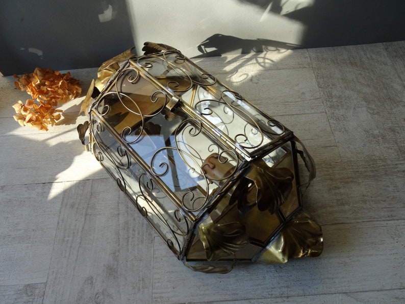 May include: A gold-toned metal and glass display case with ornate scrollwork and leaf accents. The case has a hinged lid and is perfect for displaying small items.