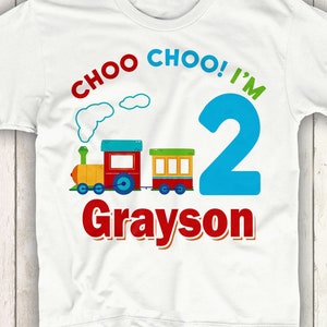 May include: White t-shirt with a red train, blue number 2, and the text "Choo Choo! I'm Grayson".