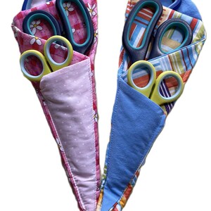 May include: Two fabric scissor holders, one pink with white daisy print and the other with a colourful striped pattern. Each holds several pairs of scissors with blue and yellow handles.