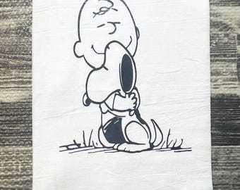 May include: Black and white illustration of Charlie Brown hugging Snoopy. The illustration is on a white kitchen towel.