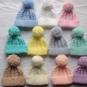 May include: Ten knitted baby hats with pom-poms in various pastel colors, including pink, blue, yellow, green, and white.