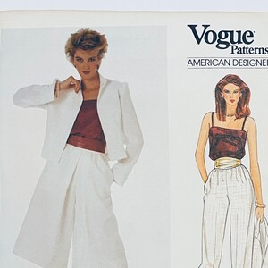 May include: Vogue Patterns American Designer sewing pattern for a white pantsuit. The pattern includes a white jacket, white pants, and a burgundy top. The pattern number is 2923. The designer is Edith Head.