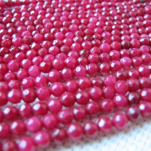 May include: Close-up of multiple strands of faceted, round, deep red beads. The beads are strung together, creating a textured surface. The beads are uniform in size and shape, with a glossy finish. The overall effect is a rich, vibrant display of color and texture.