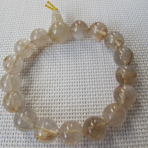 May include: A bracelet made of translucent, round beads with golden inclusions. The beads are strung together, forming a circular shape. The bracelet is a neutral colour and appears to be made of natural stone. The beads are approximately 1 cm in diameter.