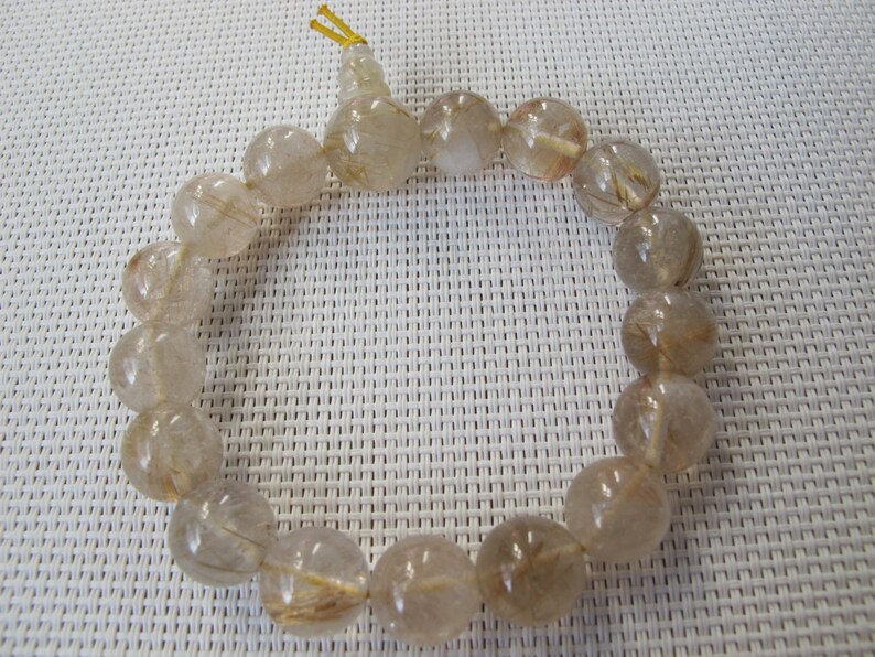 May include: A bracelet made of translucent, round beads with golden inclusions. The beads are strung together, forming a circular shape. The bracelet is a neutral colour and appears to be made of natural stone. The beads are approximately 1 cm in diameter.