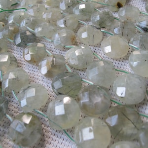 Puede incluir: Primer plano de una colección de cuentas facetadas de piedra preciosa verde pálido ensartadas en hilo verde. Las cuentas son translúcidas con inclusiones internas, dispuestas para la creación de joyas.