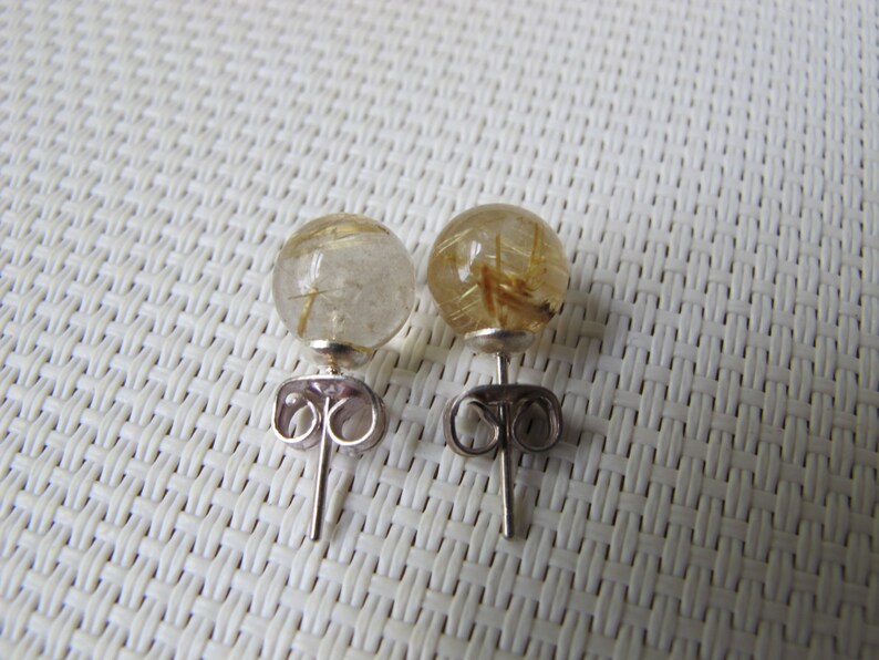Pode incluir: Um par de brincos de press&atilde;o com pedras preciosas esf&eacute;ricas transparentes com inclus&otilde;es douradas. Os brincos t&ecirc;m pinos prateados e fechos de borboleta. As pedras preciosas t&ecirc;m aproximadamente 1,3 cm de di&acirc;metro.