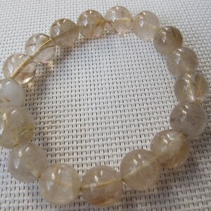 May include: A bracelet made of translucent, round beads with golden inclusions. The beads are strung together, forming a circular shape. The bracelet is a light, neutral colour, suitable for everyday wear.