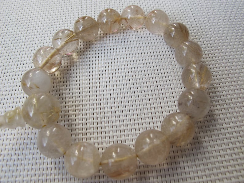 May include: A bracelet made of translucent, round beads with golden inclusions. The beads are strung together, forming a circular shape. The bracelet is a light, neutral colour, suitable for everyday wear.