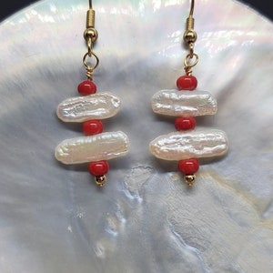 Puede incluir: Un par de pendientes de oro con tres perlas barrocas blancas y cuentas rojas en cada pendiente.