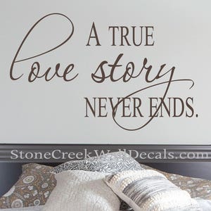 May include: A brown vinyl wall decal with the text "A true love story never ends." The decal is on a white wall above a bed with a patterned comforter and pillows.