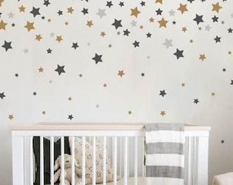 May include: A white crib with a gray and white striped blanket and a stuffed animal inside. The crib is in a nursery with a white dresser and a gray rug. The wall is decorated with gold and gray star stickers.