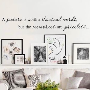 May include: A white couch with black and white pillows in a living room with a quote on the wall that reads "A picture is worth a thousand words, but the memories are priceless..."