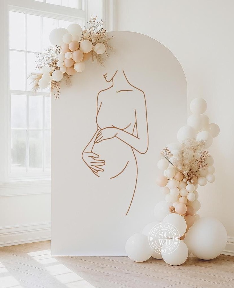May include: A large, arched, off-white display panel featuring a brown line-art illustration of a pregnant torso. The panel is decorated with clusters of white and beige balloons and dried foliage. A circular logo reads Stone Creek Wall Decals.