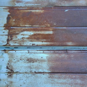 May include: Close-up of a rusty metal surface with a blue-grey paint finish. The surface is made of corrugated metal panels, creating a textured look. The rust is visible in patches, giving the surface a weathered and aged appearance.