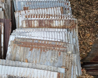 Puede incluir: Una pila de láminas de metal corrugado con una pátina oxidada y pintura blanca. Las láminas están apiladas en un patrón escalonado y tienen una textura ondulada. La lámina inferior tiene un sello circular con el texto "U.S. STEEL" en su interior.