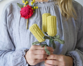 Può includere: Un mazzo di fiori gialli all'uncinetto con foglie verdi, tenuto nelle mani di una persona. I fiori sono fatti per assomigliare a fiori di Banksia.