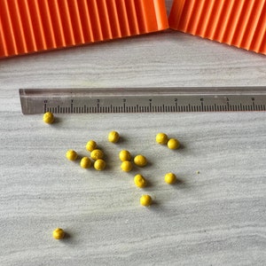 May include: A close-up of a white surface with a clear ruler and a scattering of small, yellow, round beads.