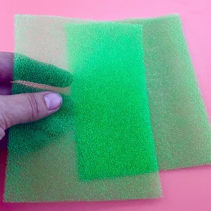 Puede incluir: Dos estropajos verdes, uno encima del otro, con un tono verde ligeramente más oscuro en el estropajo superior.