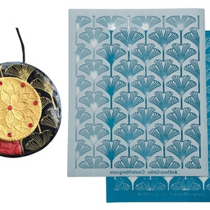 May include: A handcrafted pendant with a black cord, showcasing a gold floral design with red accents on a black, red, and gold circular base. Two Art Deco stencils with a blue fan pattern are also shown.