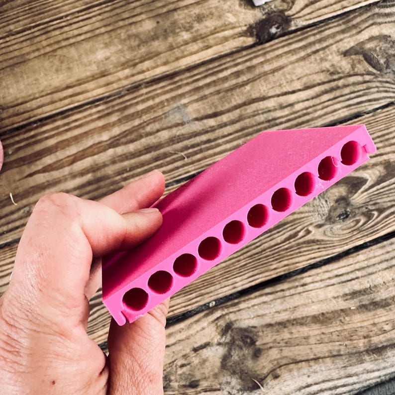 May include: A pink plastic mold with ten round holes. The mold is designed for making small objects, such as candles or soap.
