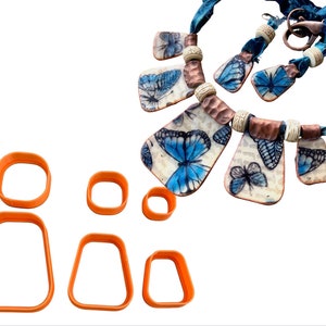 May include: Set of five orange plastic cookie cutters in different shapes, including a rectangle, a square, and two ovals. The cutters are arranged in a row on a white background.
