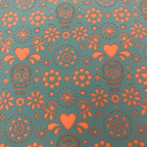 May include: Teal fabric featuring a repeating pattern of orange sugar skulls, hearts, and floral motifs. The design is cut out, creating a textured effect. The theme is reminiscent of the Day of the Dead celebrations.