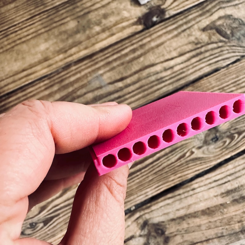 May include: A pink plastic mold with ten round holes. The mold is designed for creating small objects.