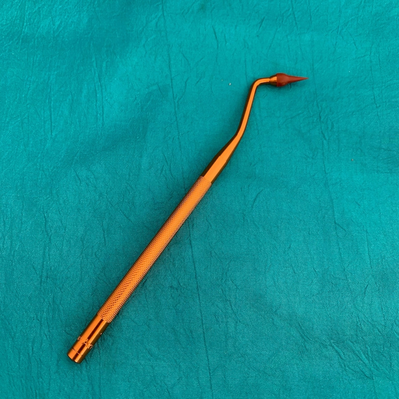 May include: A gold-colored dental tool with a curved, pointed tip. The tool is designed for cleaning and removing plaque from teeth.