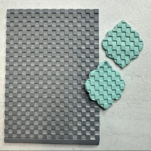 May include: A gray rectangular textured mat with a woven pattern, next to two turquoise, quatrefoil-shaped objects with a similar woven design. The objects are likely decorative or functional, possibly for crafts or home decor.
