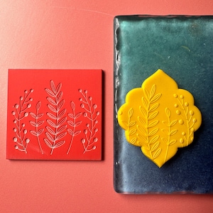 Może przedstawiać: Dwa czerwone i żółte płytki ceramiczne z wzorem kwiatowym. Płytki są ozdobione powtarzającym się wzorem stylizowanych liści i jagód.