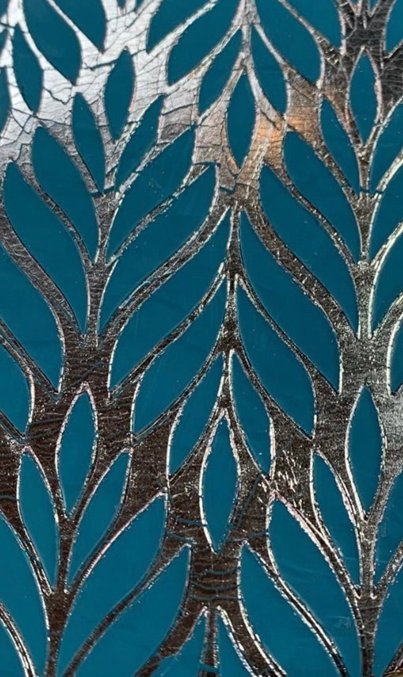 May include: A teal blue background with a silver metallic leaf pattern. The leaves are arranged in a repeating pattern, creating a decorative design.