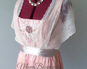 May include: A pink satin dress with a white lace overlay and a satin sash. The dress features a floral design on the bodice and a scoop neckline.