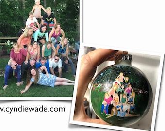 May include: A hand-painted Christmas ornament featuring a family of 16 people in a pyramid formation, reminiscent of a family photo. The ornament is round and white with a green background. The family is depicted in a variety of colors and poses, with a green tree in the background.