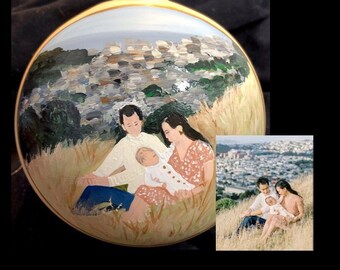 May include: Hand-painted Christmas ornament featuring a family of three, a man, a woman, and a baby, sitting in a field with a city skyline in the background. The ornament is painted in a realistic style with muted colors.